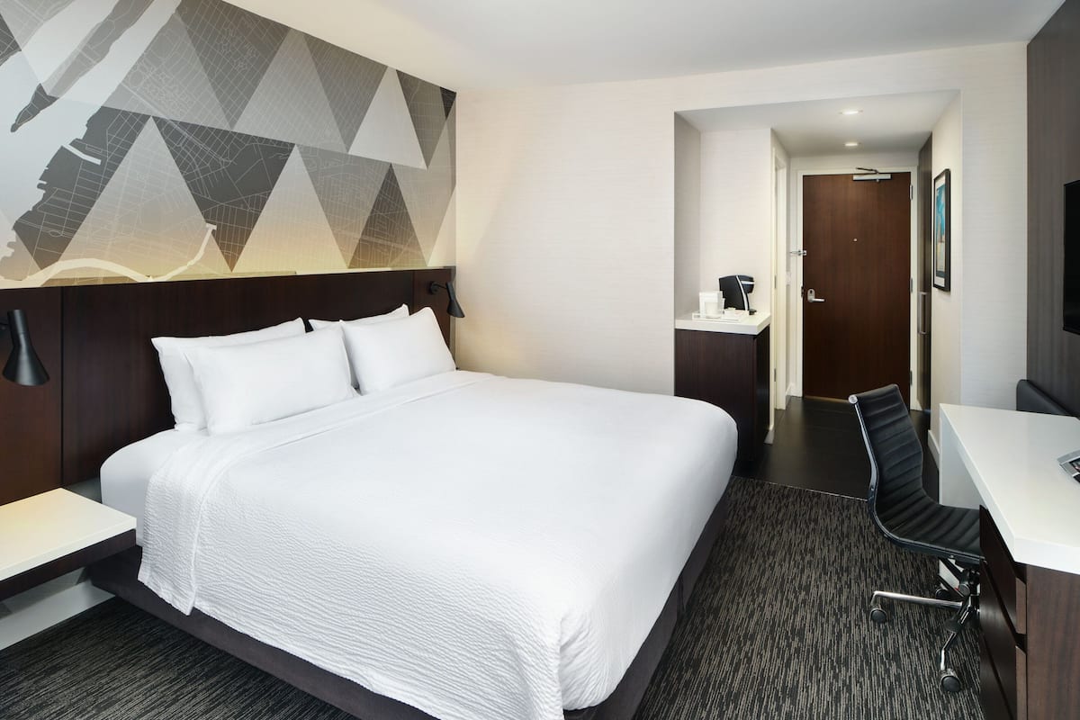 A hotel room with a large bed, a desk, a chair, and a wall-mounted TV.