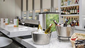 Uma área de bar com bancada de mármore, um balde de metal com garrafas e uma taça de vinho.