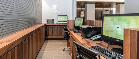 A modern office space with multiple computer workstations, a wooden reception desk, and a wall-mounted printer.