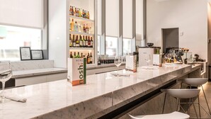 Uma área de bar moderna com bancada de mármore, banquetas e diversos frascos nas prateleiras.