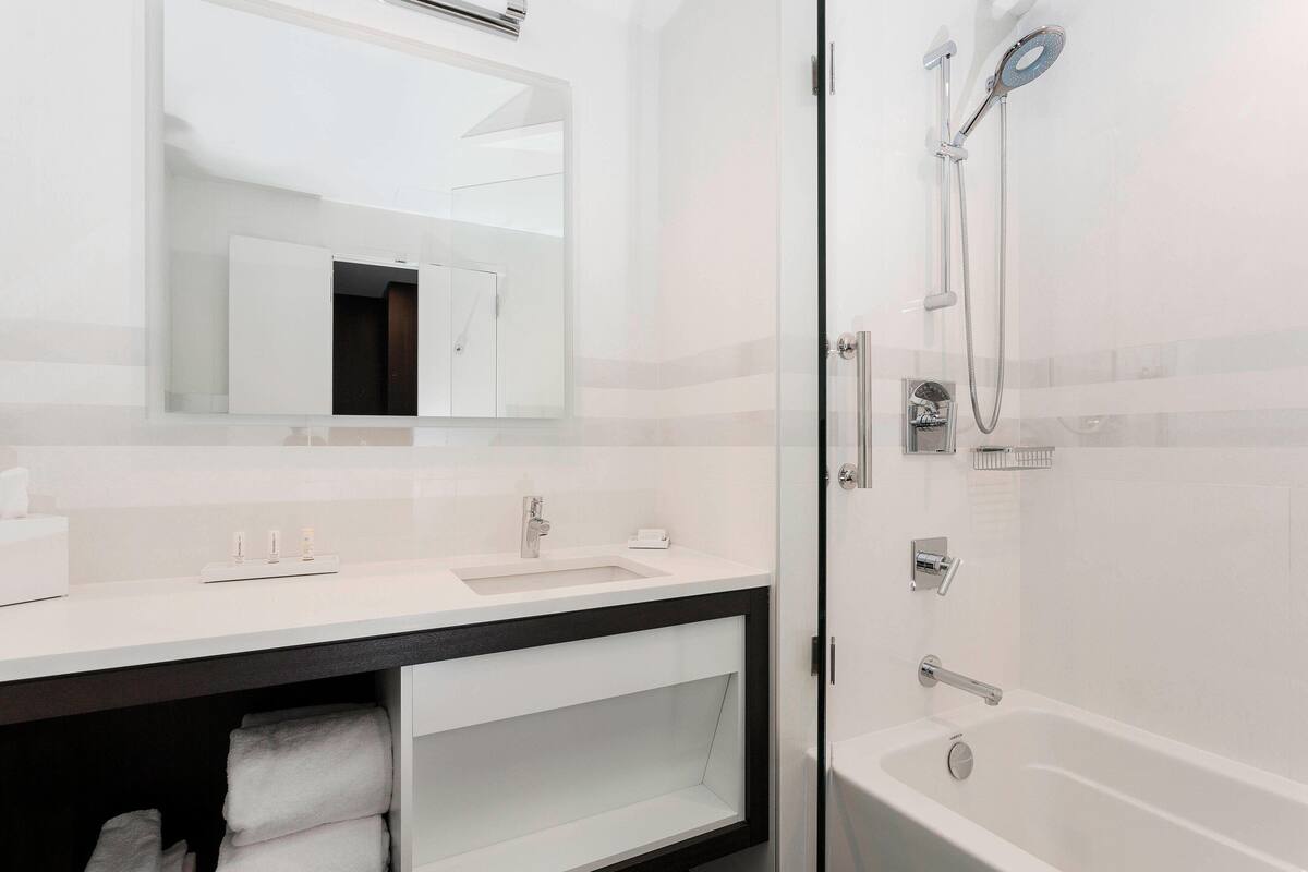 Een moderne badkamer met een witte wastafel, een spiegel erboven en een douchegedeelte met een handdouche.