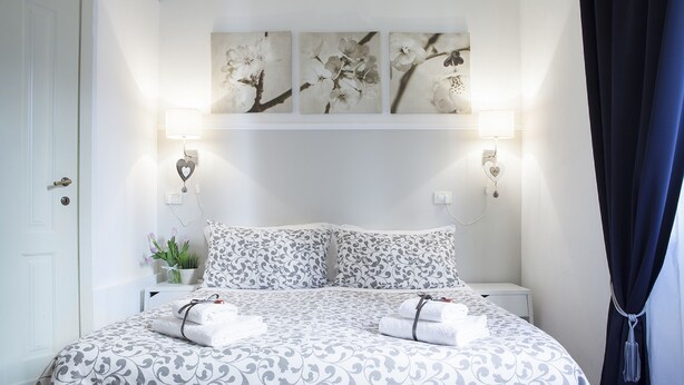 Una cama bien tendida con ropa de cama estampada, una planta en la mesita de noche y lámparas fijadas a la pared.