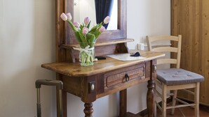 Un escritorio de madera con un espejo, una silla, una mesita y una maleta.