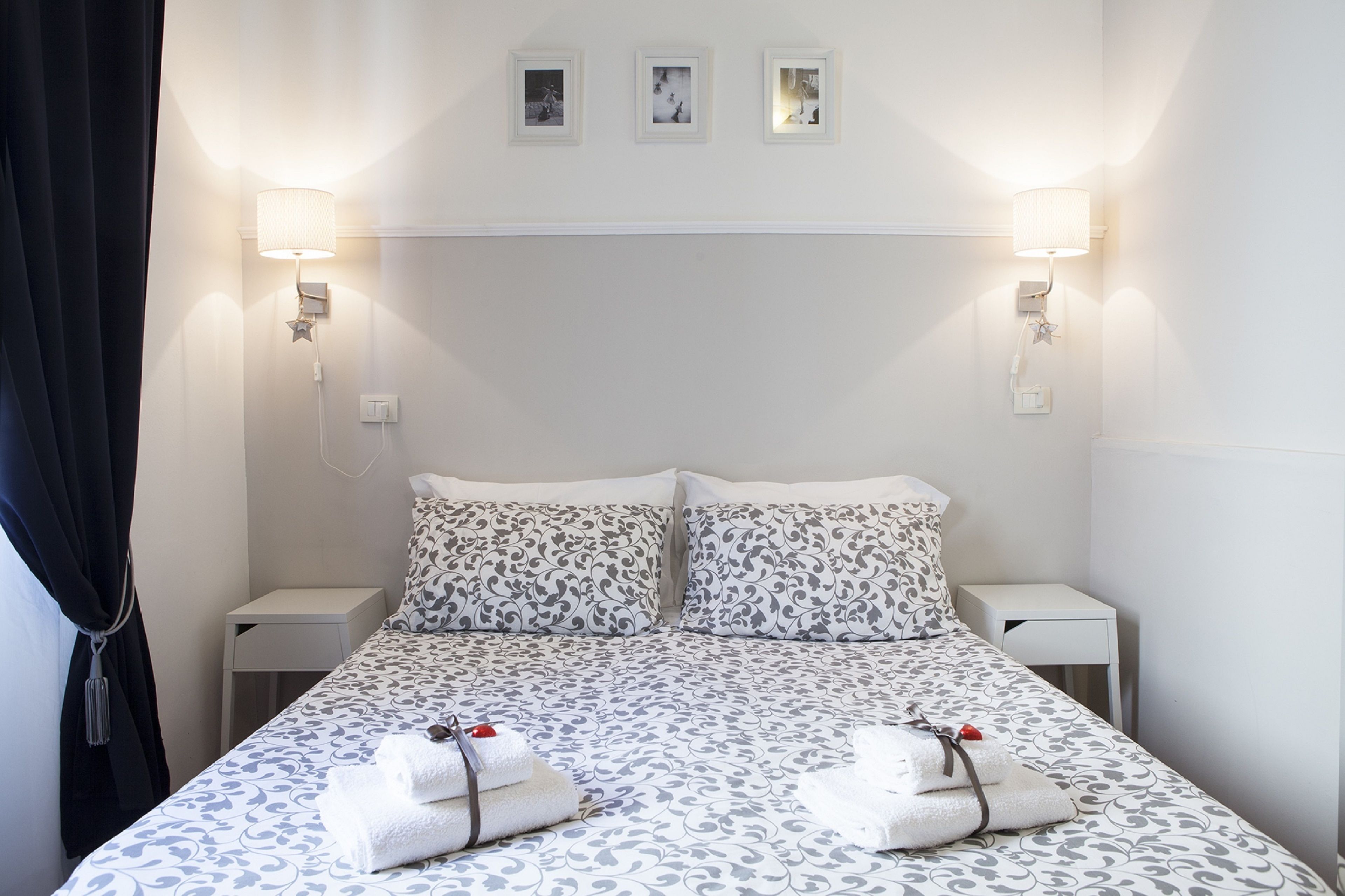 A neatly made double bed with patterned bedding, two bedside tables, and wall-mounted lamps.