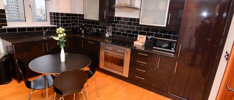 A modern kitchen with black cabinets, a stainless steel oven, and a dining area with a round table and chairs.