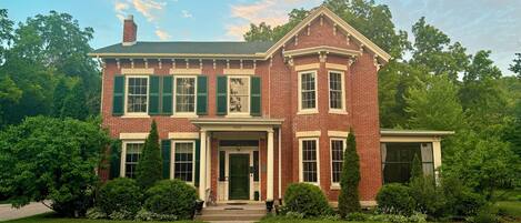 A two-story brick house with a front porch, green shutters, and a number '900' on the front door.