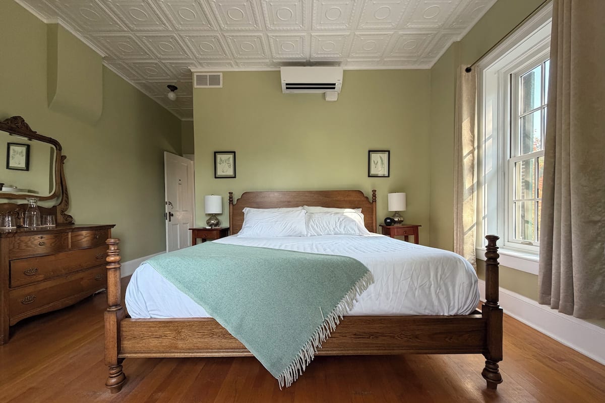 A neatly made bed in a room with a wooden headboard, a green throw blanket, and a wooden dresser with a mirror.