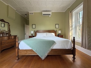 Een opgemaakt bed in een kamer met een houten hoofdbord, een groene plaid en een houten dressoir met spiegel.