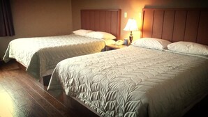Camera d'albergo con due letti, pavimento in legno, un comodino con lampada e un telefono.