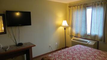 Una camera d'albergo con un letto, una televisione, una scrivania, una lampada e una finestra con tende.