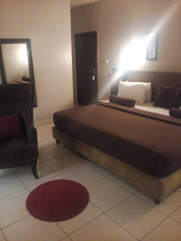 A bedroom with a bed, a chair, a door, and a mirror.