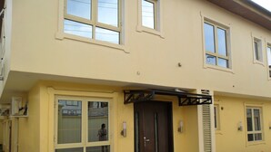 A two-story building with a yellow facade, a dark brown entrance door, and multiple windows. - Swisscottage suites (Lagos)
