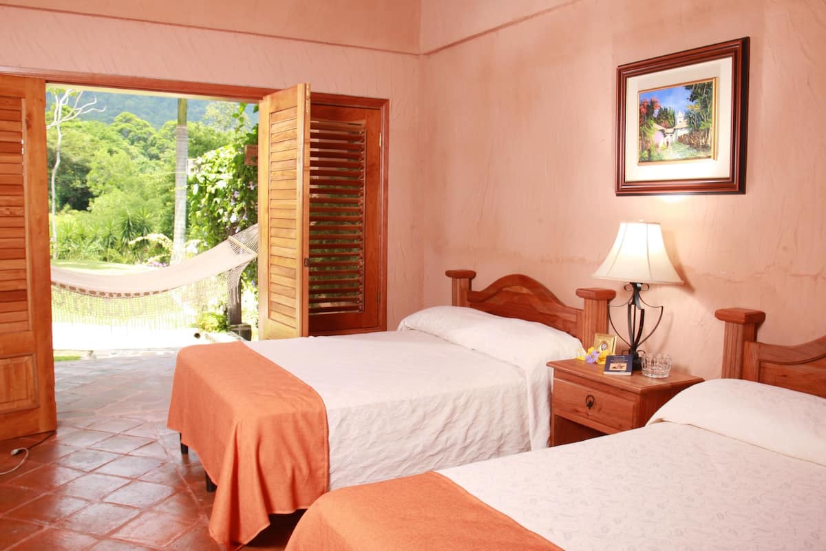 A room with two beds, a wooden headboard, a nightstand with a lamp, and a framed picture on the wall.