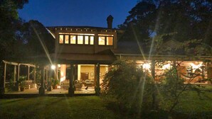 A two-story house with a covered patio area, a chimney, and a well-lit interior. - La Villa de Soledad B&B (La Ceiba)