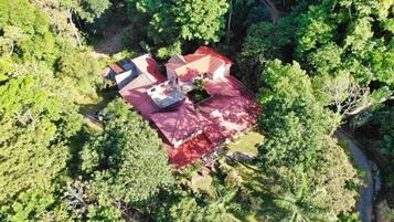 Vista aérea de una propiedad con un edificio de techo rojo rodeado de abundante vegetación.