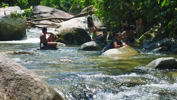 Um grupo de pessoas sentadas em pedras em um rio corrente, cercado por grandes rochas e vegetação.