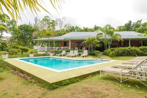 A rectangular pool with a tiled deck, surrounded by lounge chairs and potted plants.