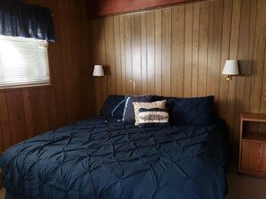Cozy retreat with a dark blue quilted bedspread, wooden headboard, and two bedside lamps.
