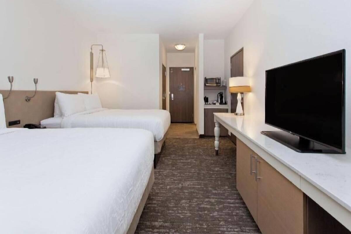 A hotel room with two beds, a TV, a desk, and a kitchenette.