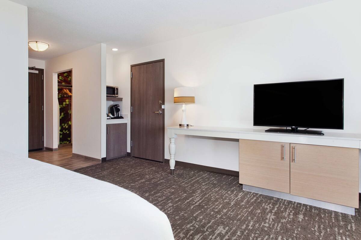 A hotel room with a bed, a TV on a white console, a desk, and a wardrobe.