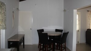 A dining area with a round table and chairs, a bench, and a door. - Fitz Aruba 2 Bedroom Home (Noord)