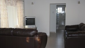 A living room with two leather sofas, a television on a stand, and a bathroom visible through an open door. - Fitz Aruba 2 Bedroom Home (Noord)