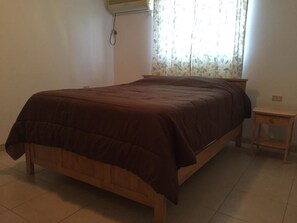 A single bed with a brown bedspread in a room with a tiled floor and a small wooden nightstand. - Fitz Aruba 2 Bedroom Home (Noord)