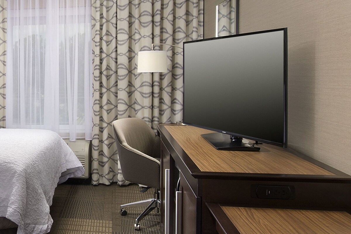 Ein Hotelzimmer mit einem Bett, einem Schreibtisch mit Fernseher, einem Sessel und einer Lampe.
