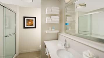 A modern bathroom with a glass shower enclosure, a large mirror, and neatly arranged towels on shelves.