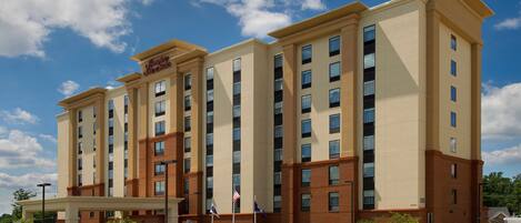 Un hôtel à plusieurs étages, avec une façade beige et marron, des drapeaux américains et un ciel d’un bleu limpide.