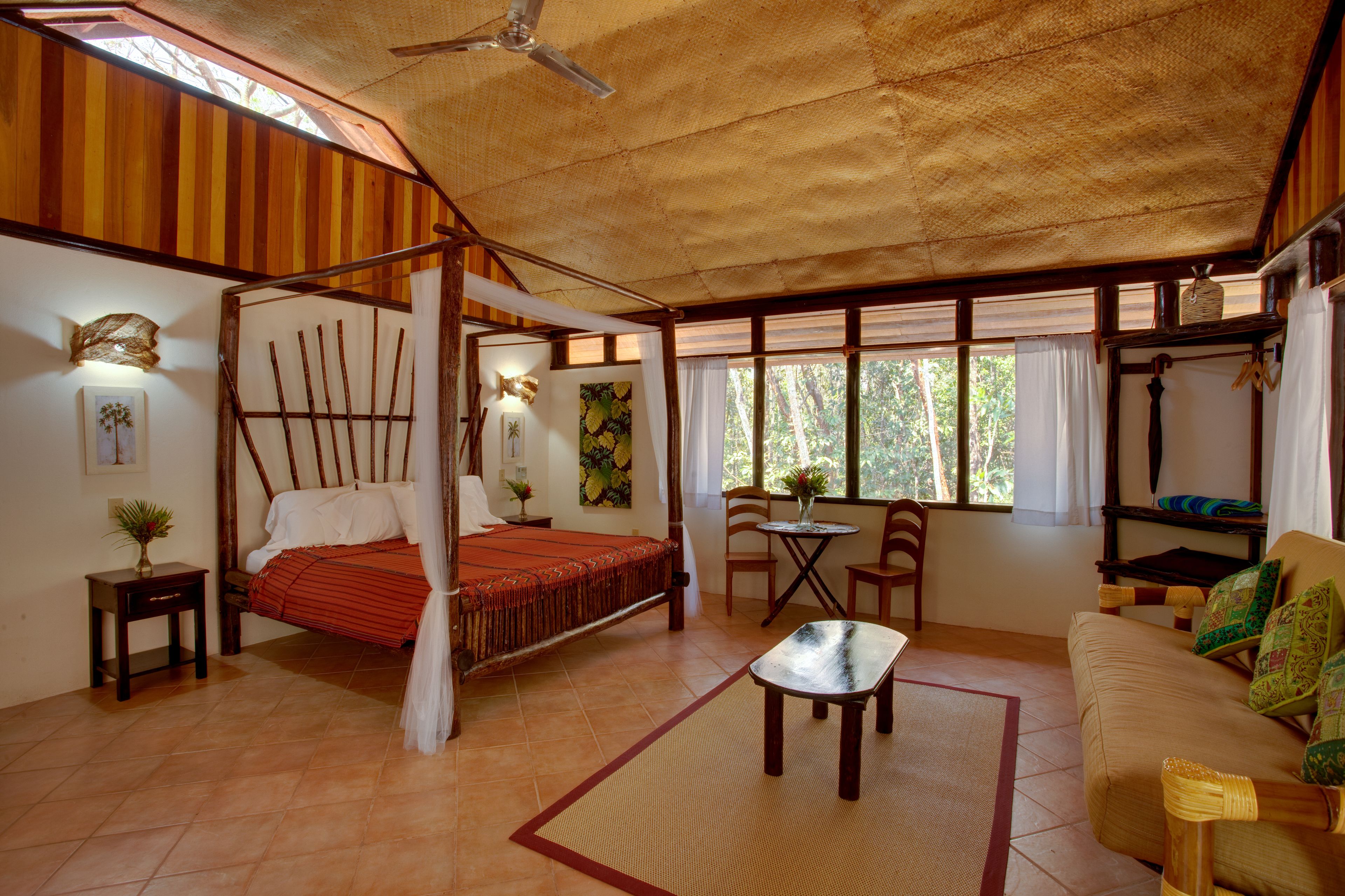 Una habitación con cama con dosel, un sofá, una mesita y un ventilador de techo.