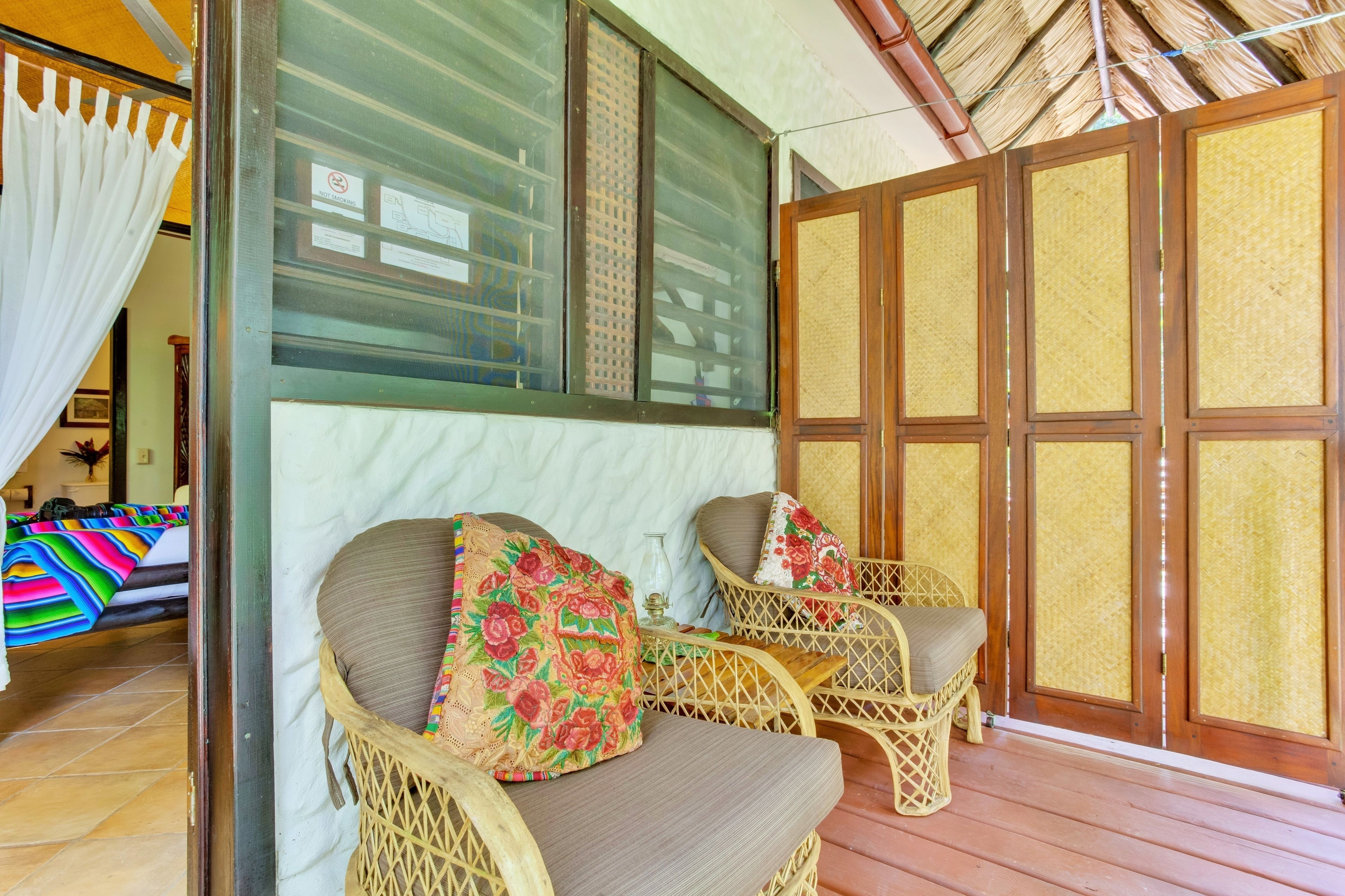 A room with wicker furniture, a bed with a colorful blanket, and a large window with a view.