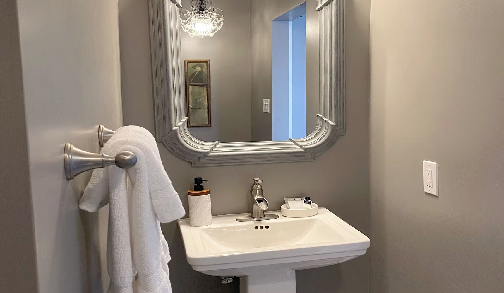 Une salle de bain avec un lavabo blanc, un miroir, un porte-serviettes et un lustre.