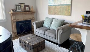 Ein Wohnzimmer mit Kamin, einem grauen Sofa, einem gemusterten Teppich und einem alten Koffer.