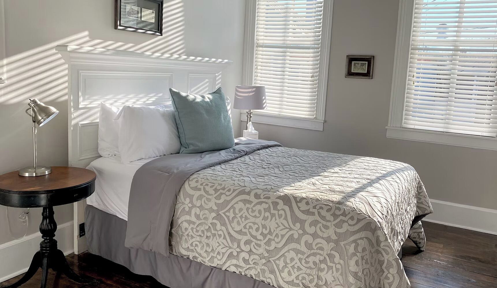 A bedroom with a bed, bedside table, lamp, and window blinds.