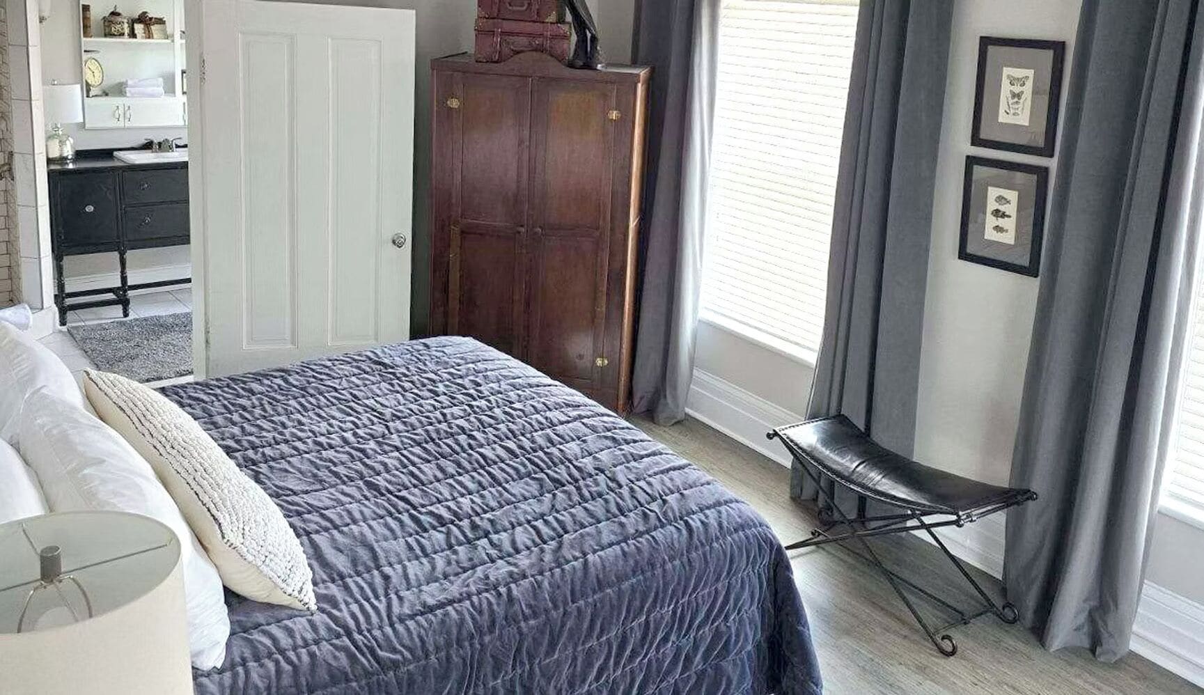 Un dormitorio con cama, cómoda, silla, ventana con cortinas y un cuadro con marcos.