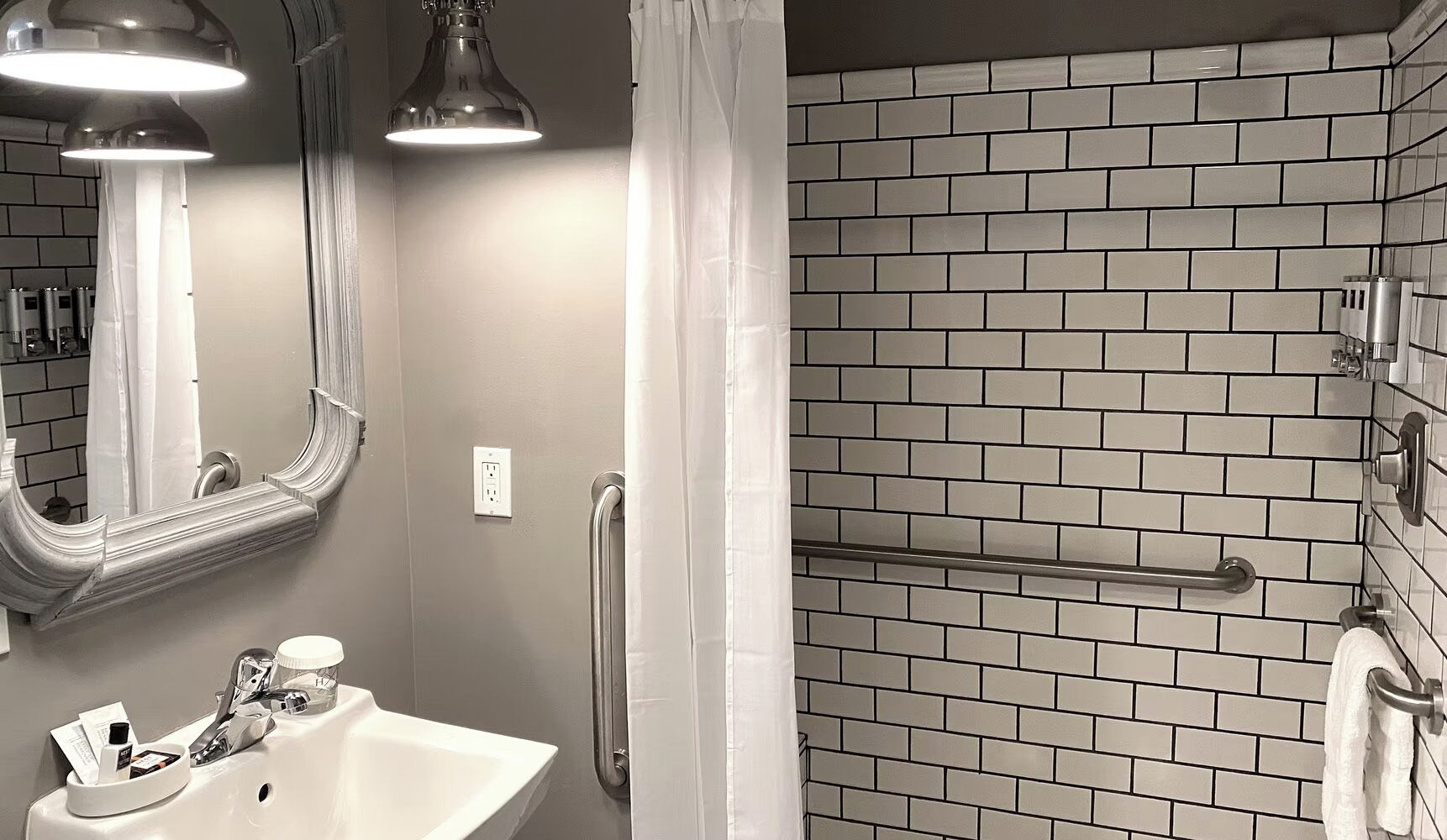 A bathroom with a sink, mirror, and a shower area with a tiled wall.
