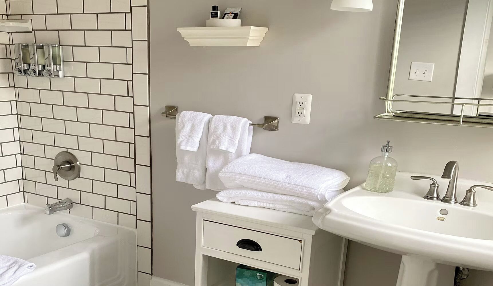 A bathroom with a bathtub, a sink, a mirror, and a towel rack.
