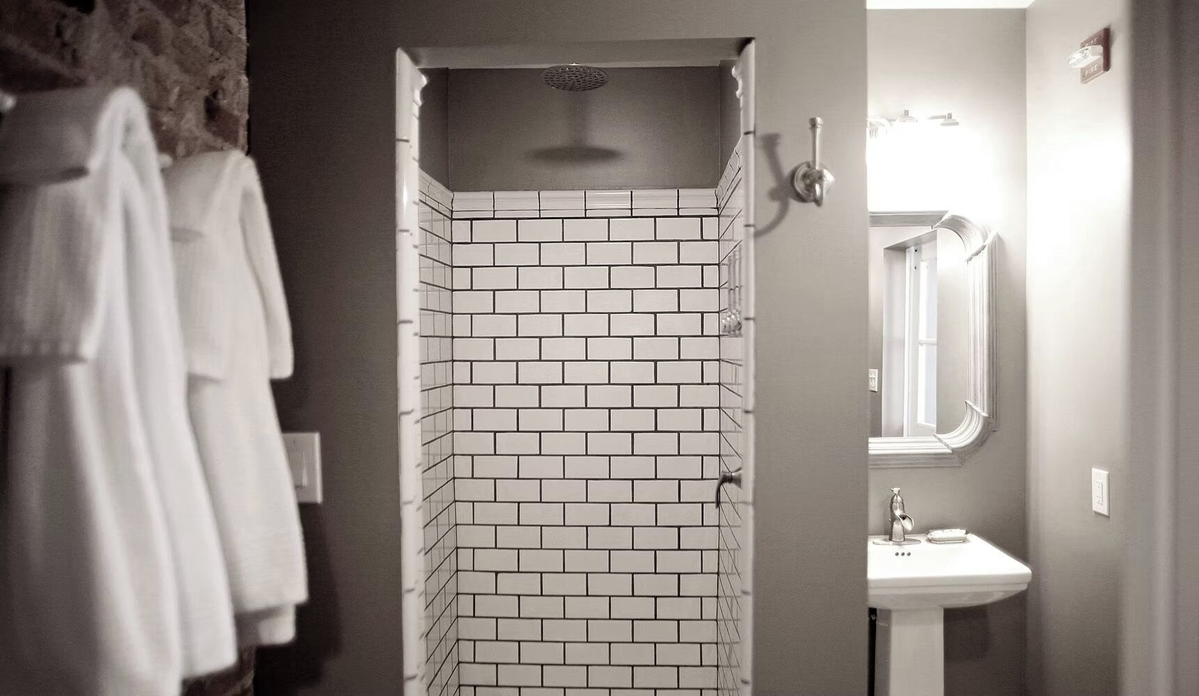 Un baño con ducha azulejada, lavamanos y espejo.