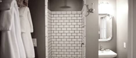 Un baño con ducha azulejada, lavamanos y espejo.