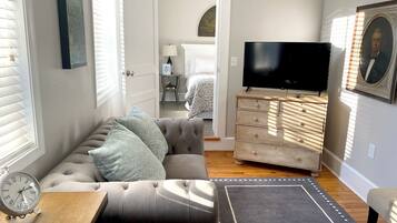 A cozy living room with a sofa, a TV, a dresser, and a clock.