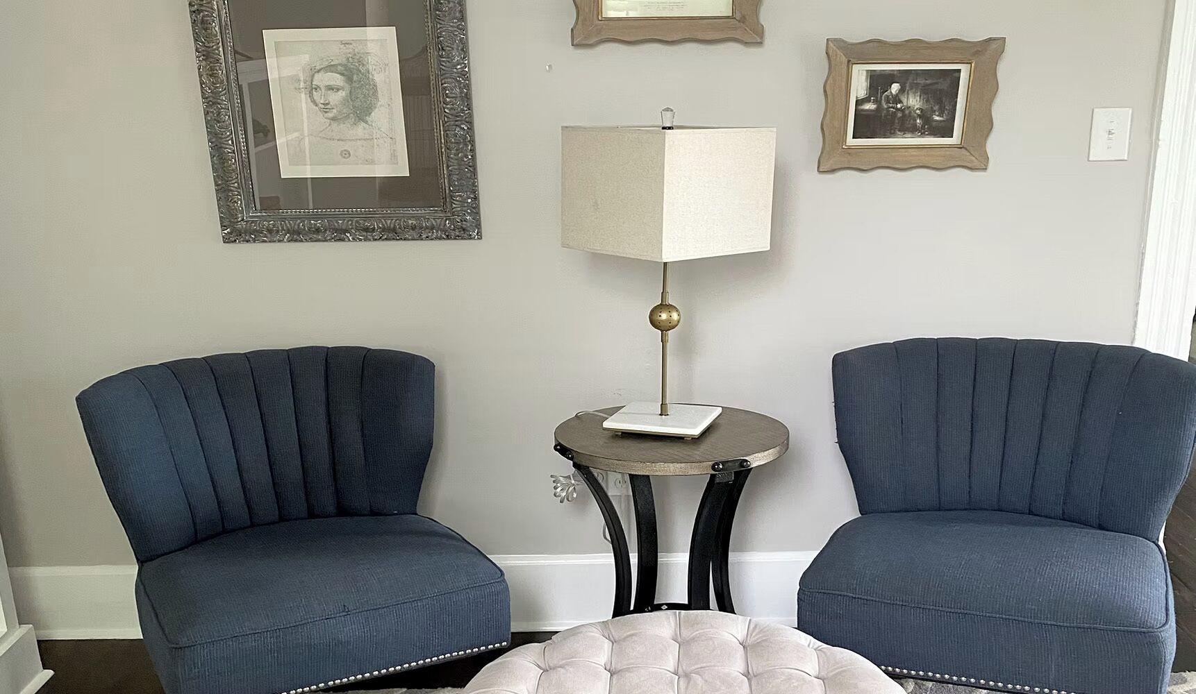 Dos sillones, una mesita de noche con una lámpara y cuadros enmarcados en la pared.