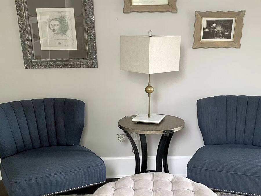 Dos sillones, una mesita de noche con una lámpara y cuadros enmarcados en la pared.