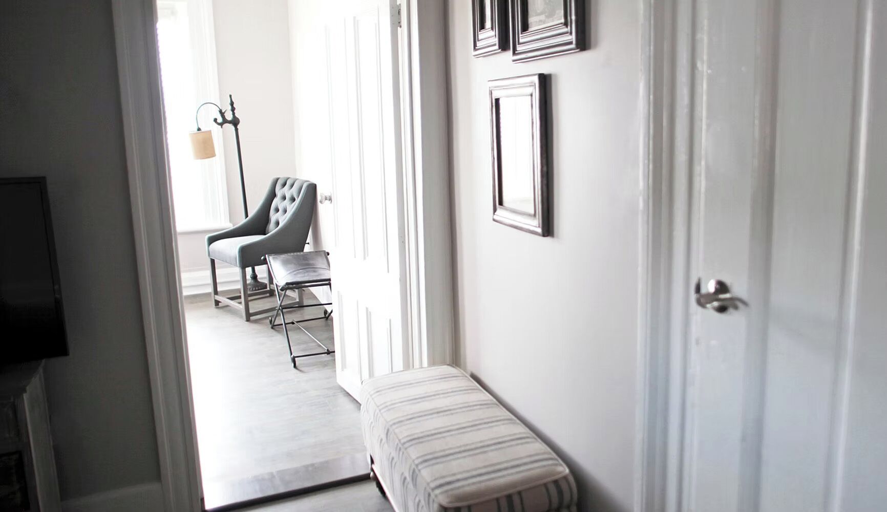 A hallway with a bench, a chair, and a door leading to a room.