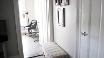 A hallway with a bench, a chair, and a door leading to a room.