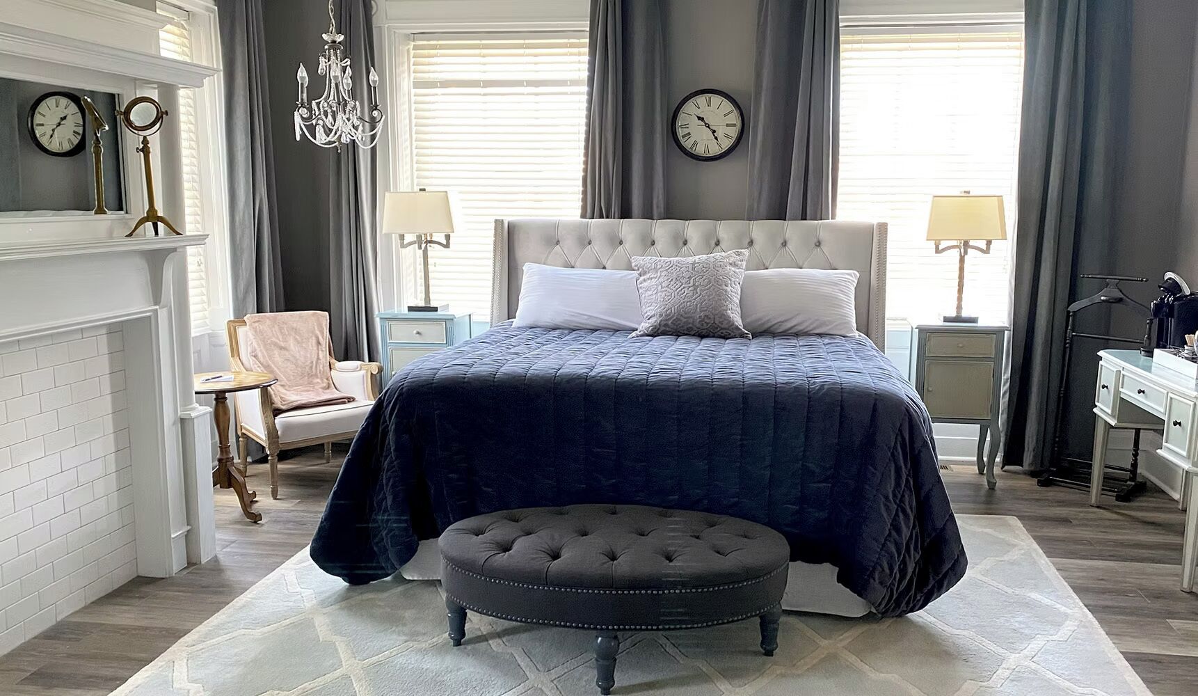 A bedroom with a large bed, two bedside tables, a chair, a dresser, a mirror, and a chandelier.