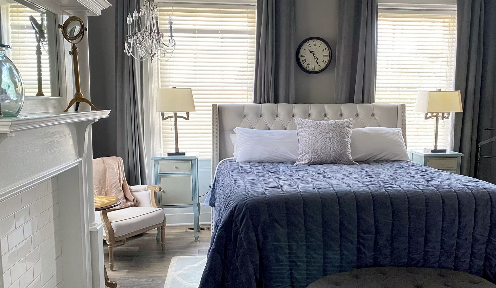 A bedroom with a large bed, a nightstand, a chair, a dresser, a clock, and a chandelier.