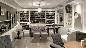Una habitación con sofá, reposapiés, sillas, una mesa y una estantería llena de libros.