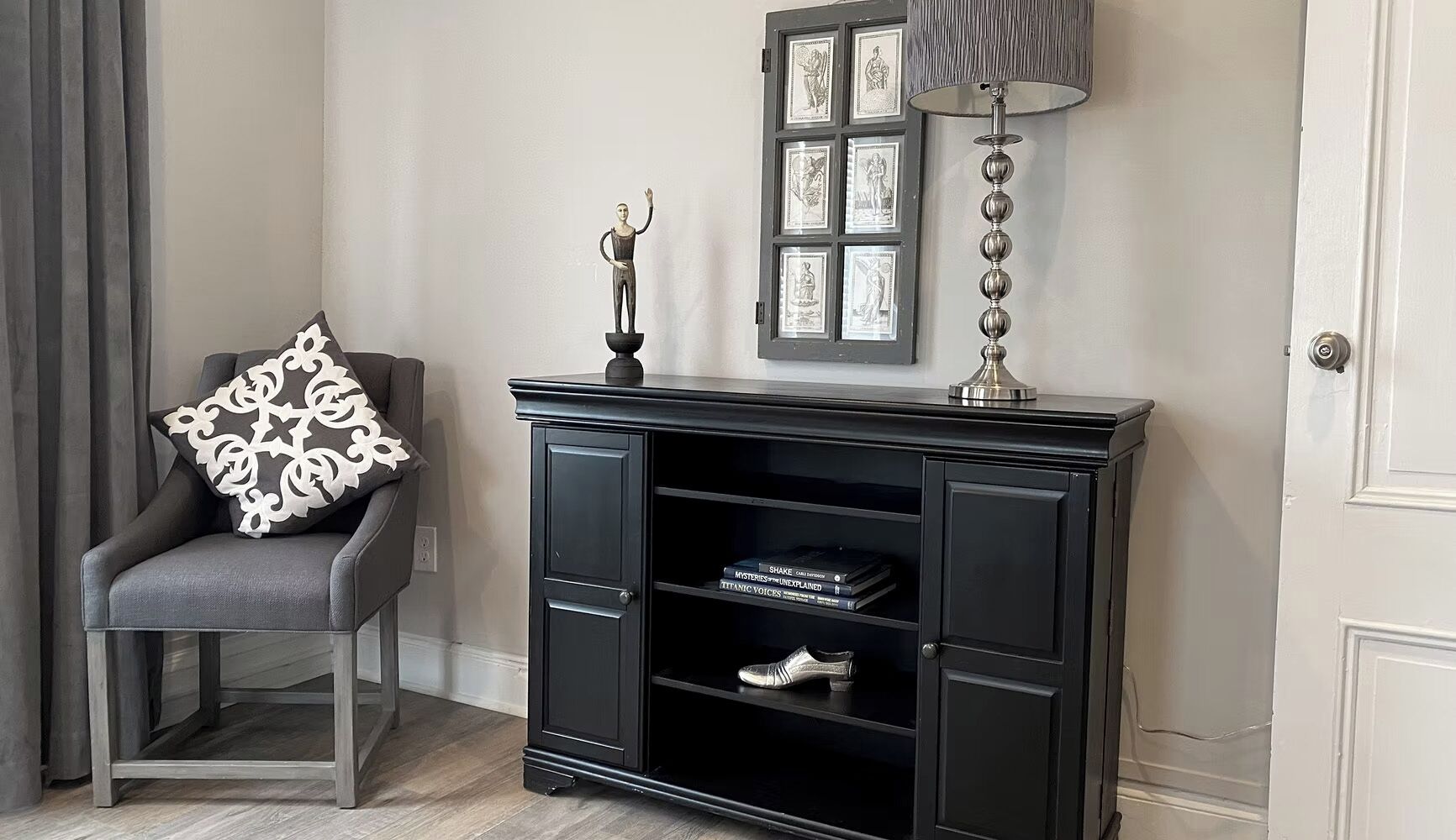 Un mueble multimedia negro con un zapato en el estante inferior, una lámpara y cuadros en la pared.