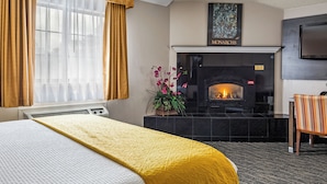 Quarto de hotel com cama, lareira, televisão e janela com cortinas.